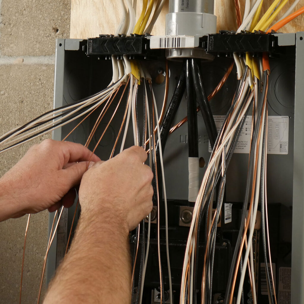 A person is working on an electrical panel, handling multiple wires connected to the system.